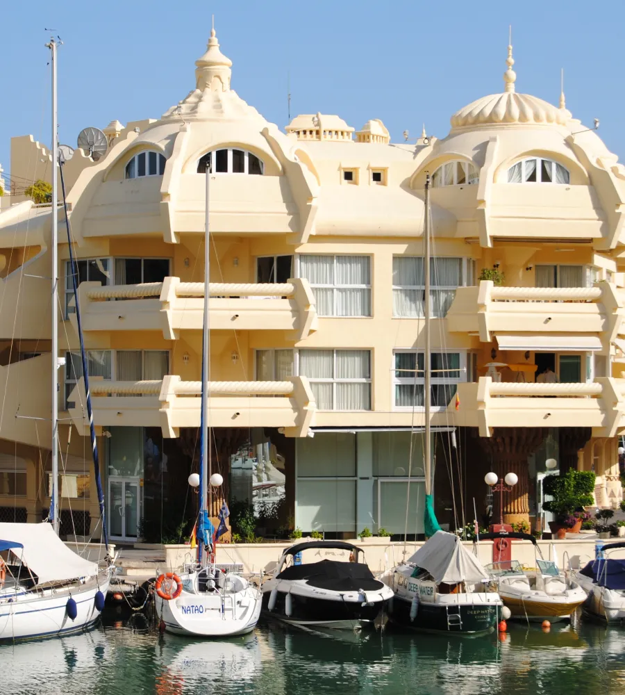 Edificio beige estilo barroco con yates atracados en un puerto.