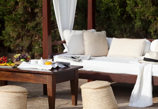 Sala exterior con sof&aacute;, mesa de madera y decoraci&oacute;n natural.