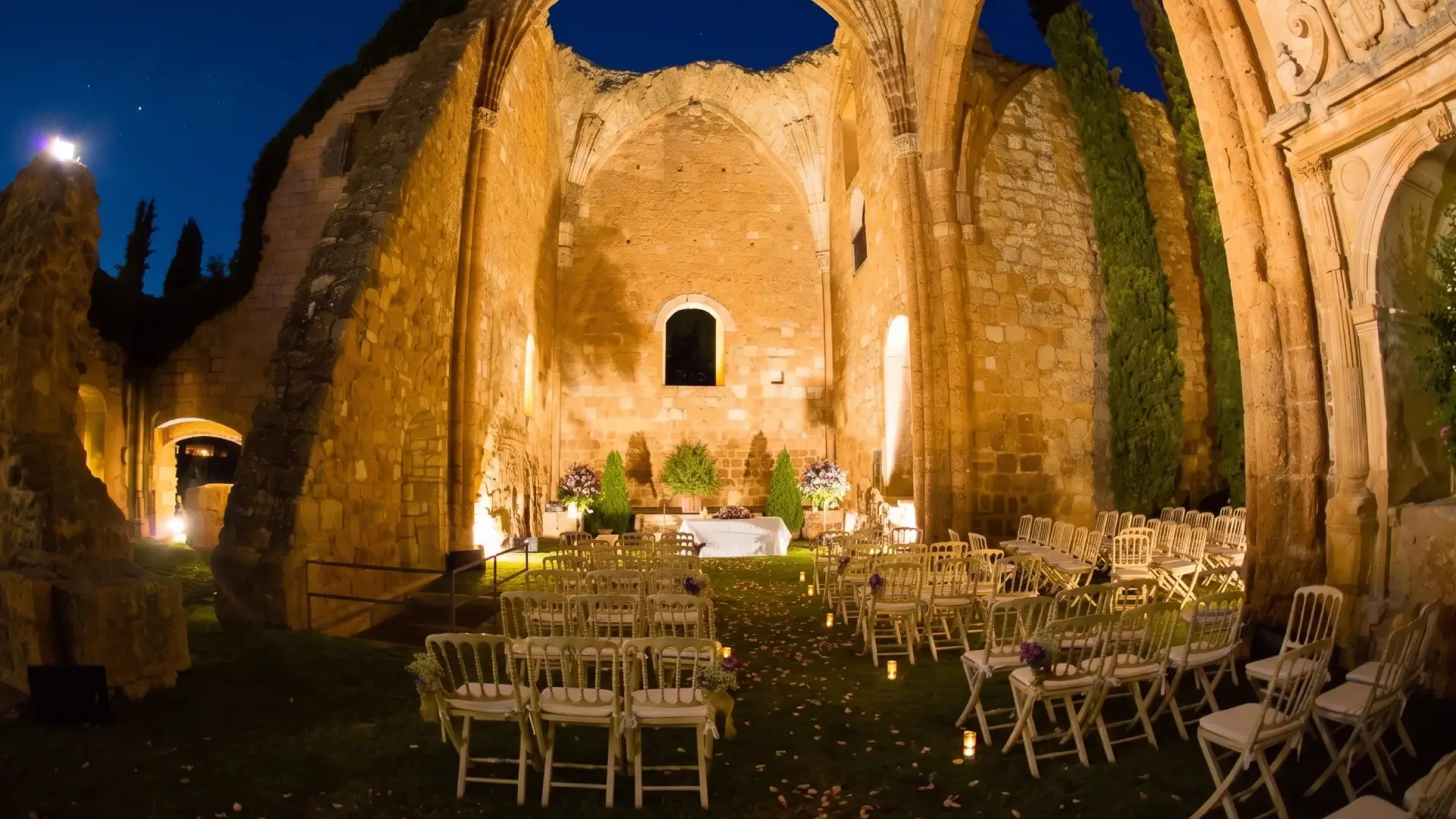 Ruinas iluminadas por la noche, preparadas para un evento con sillas dispuestas.
