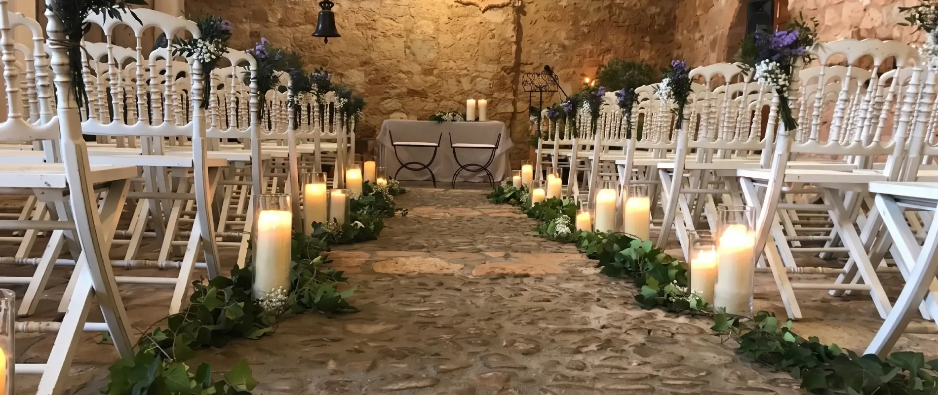 Pasillo nupcial decorado con flores y velas en un ambiente r&uacute;stico de piedra.
