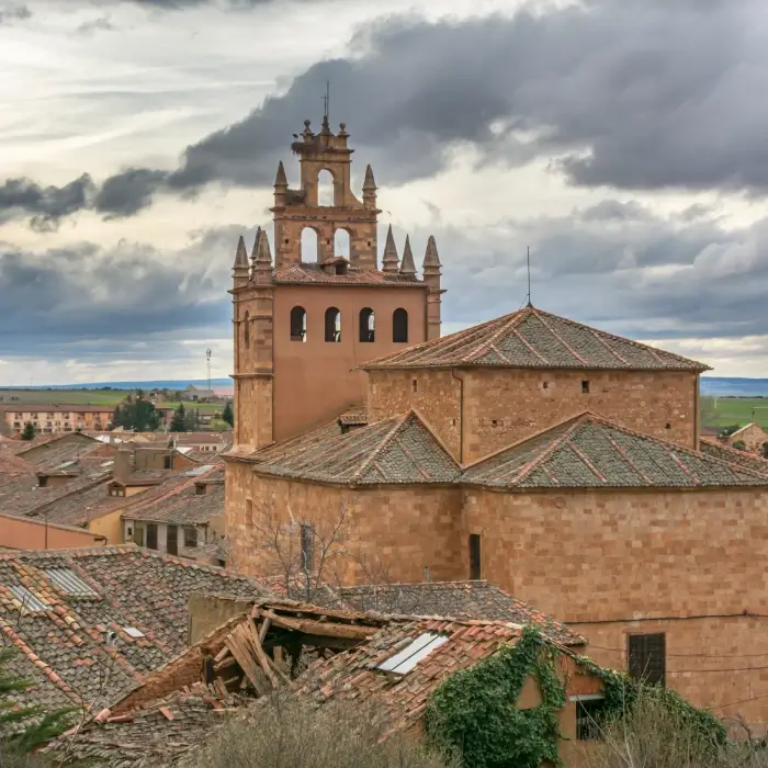 Iglesia hist&oacute;rica con cielo nublado y tejados de ladrillo alrededor.