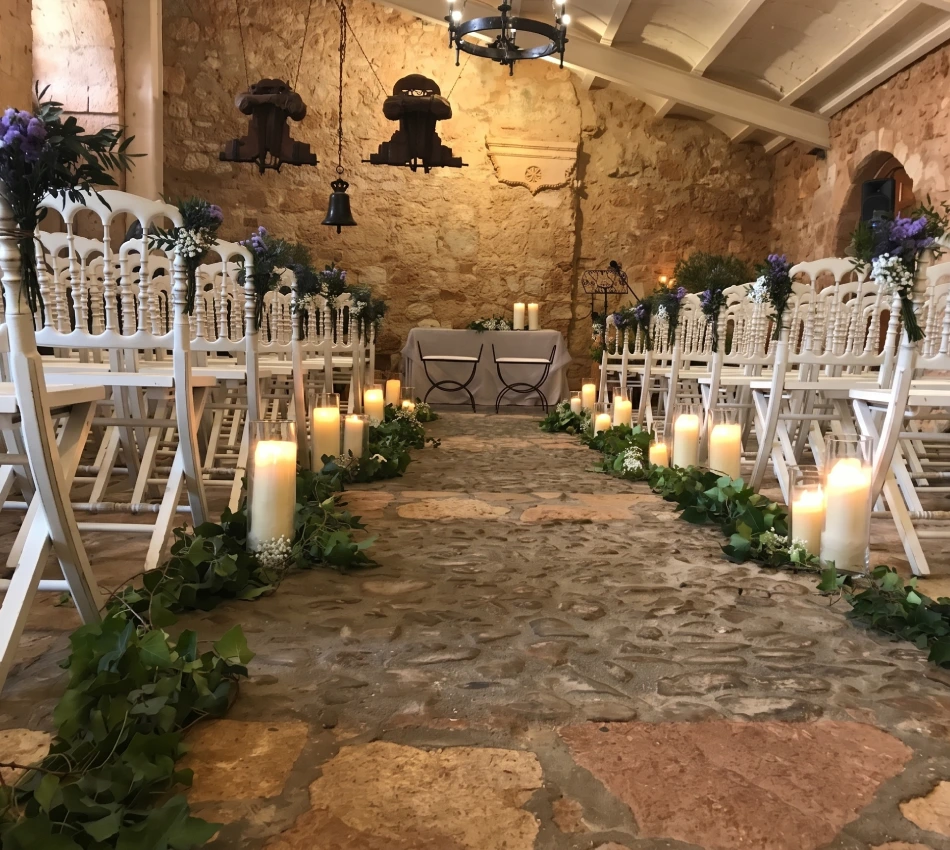 Pasillo de ceremonia decorado con velas y flores en una capilla de piedra.