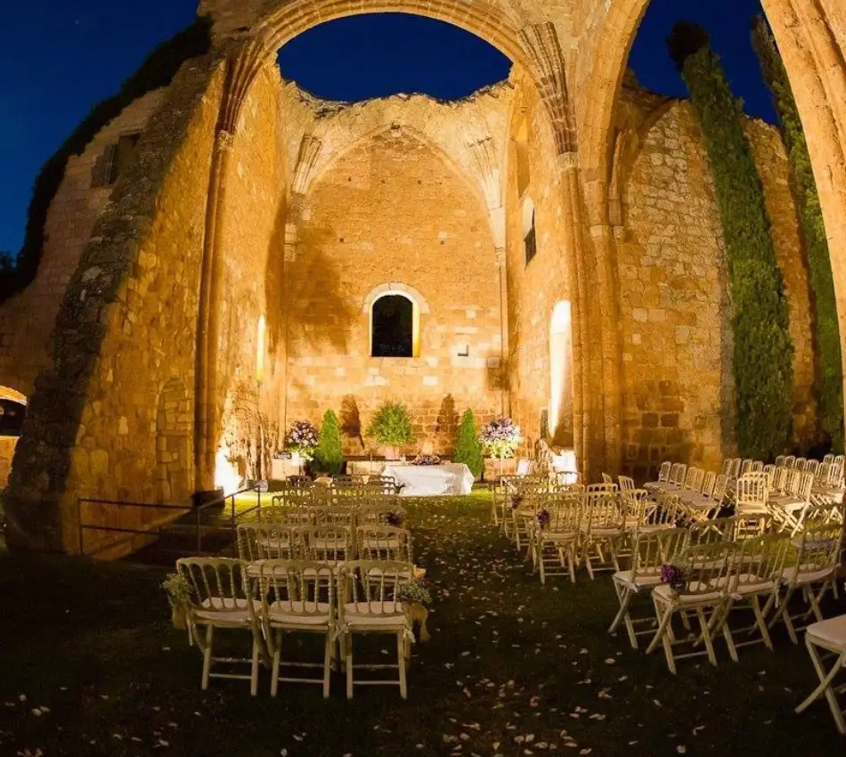 Ceremonia al aire libre en ruinas iluminadas con sillas y decoraci&oacute;n floral.