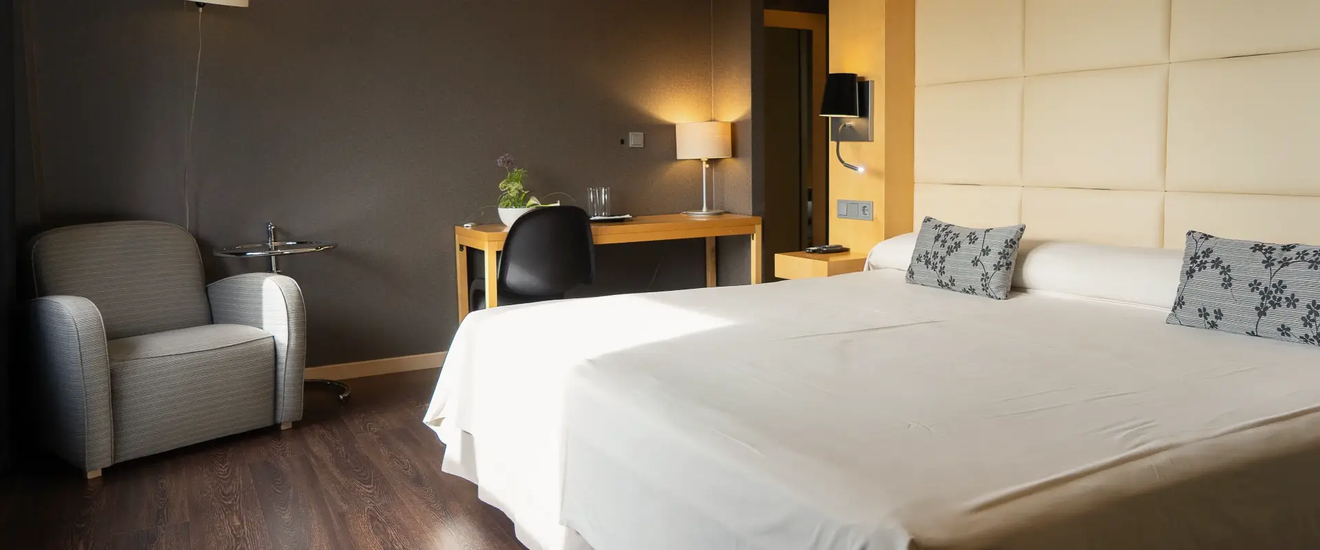Habitaci&oacute;n de hotel con cama grande, sill&oacute;n y escritorio iluminado.