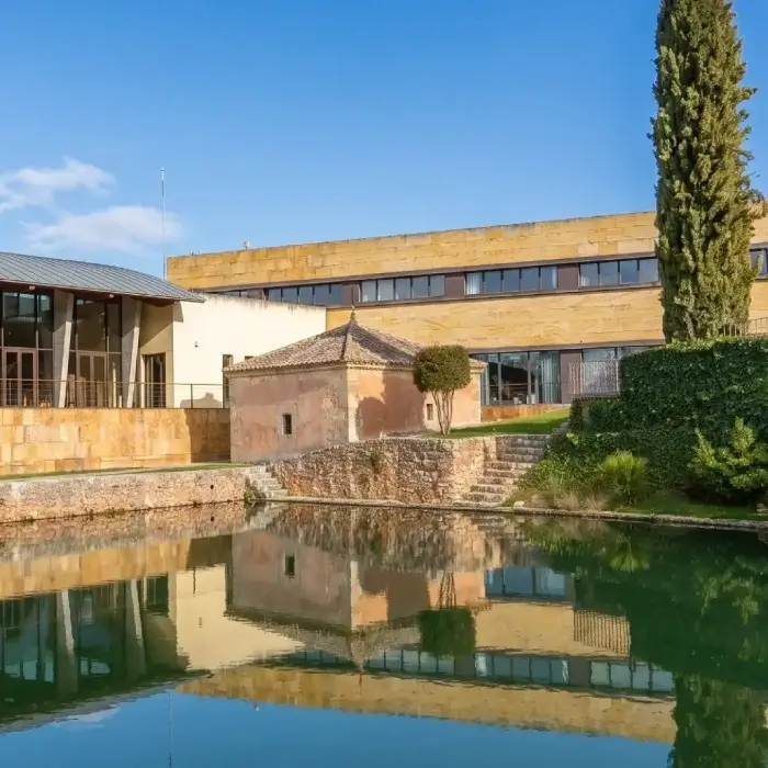 Edificio moderno junto a un estanque con su reflejo en el agua.