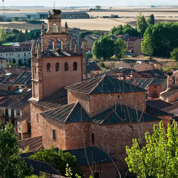 Iglesia de piedra con campanario y fondo de campos y &aacute;rboles verdes.