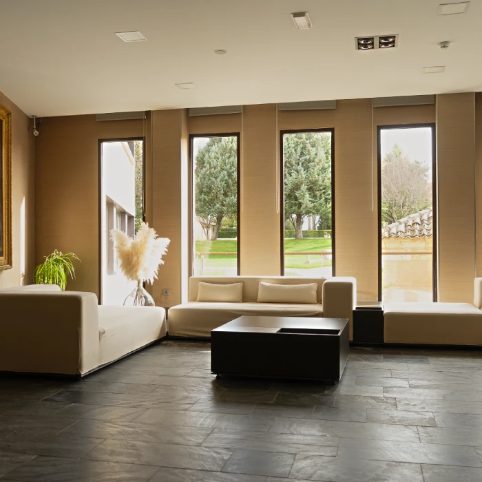 Sala moderna con sof&aacute;s claros y ventanas grandes con vistas al jard&iacute;n.