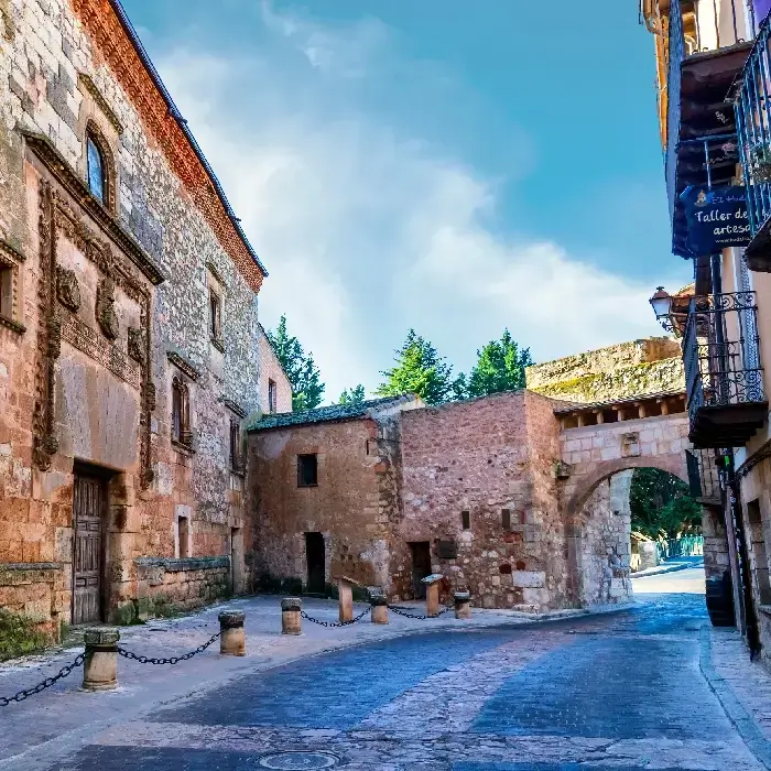 Callej&oacute;n empedrado con edificios de piedra y un arco en un d&iacute;a soleado.