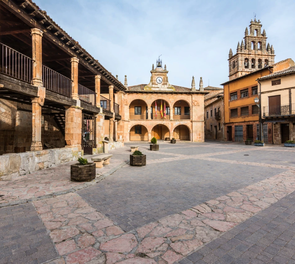 Plaza con edificios hist&oacute;ricos y torre, suelo de adoquines y cielo despejado.