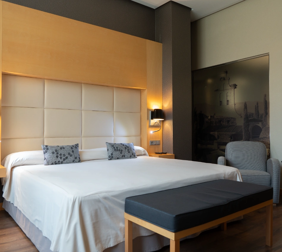 Habitaci&oacute;n de hotel moderna con cama doble, sill&oacute;n y decoraci&oacute;n minimalista.