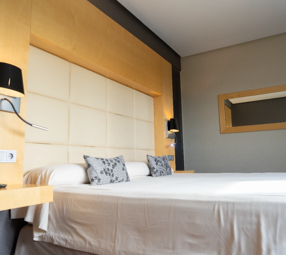 Cama con cabecero acolchado y l&aacute;mparas modernas a los lados.