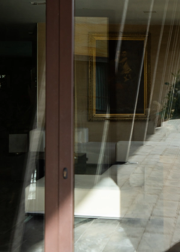 Reflejo en vidrio de una sala con arte enmarcado y un sof&aacute; blanco.