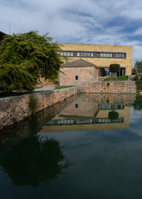 Edificio junto a un estanque con su reflejo en el agua y cielo nublado.