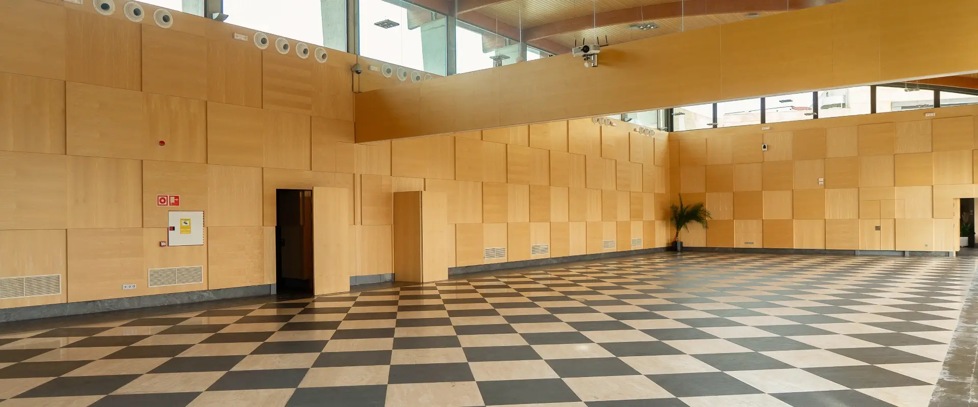Sala vac&iacute;a con suelo ajedrezado y paredes de madera clara.