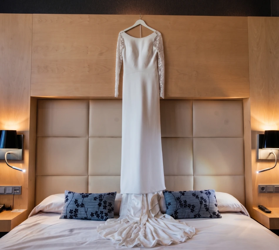 Vestido de novia blanco colgado sobre la cama de un hotel moderno.