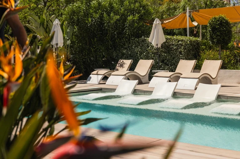 Piscina iluminada con sillas y plantas alrededor.