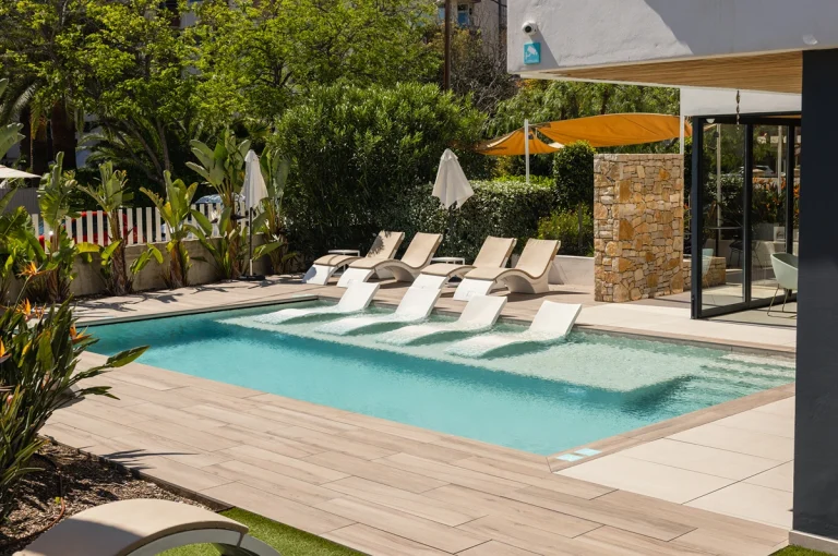 Piscina al aire libre con tumbonas y sillas modernas bajo pérgola de madera.