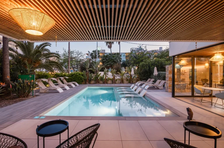 Piscina moderna con sillas de diseño bajo palmeras al fondo.