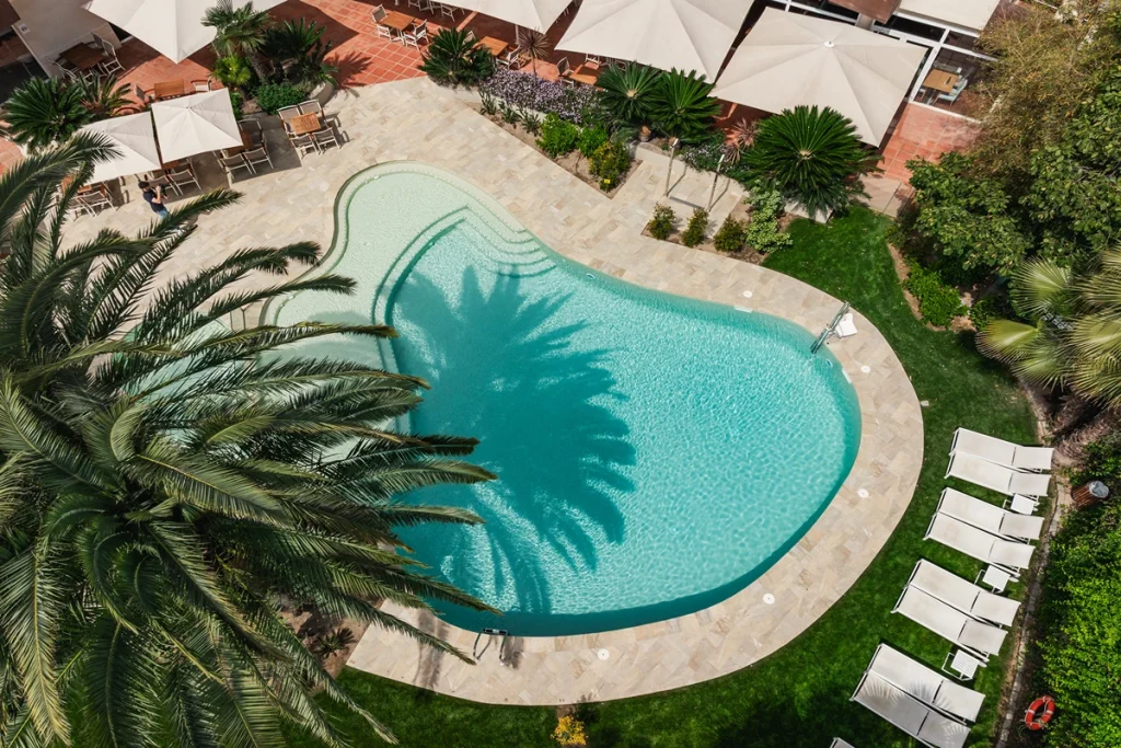 Piscina rodeada de palmeras y tumbonas blancas.