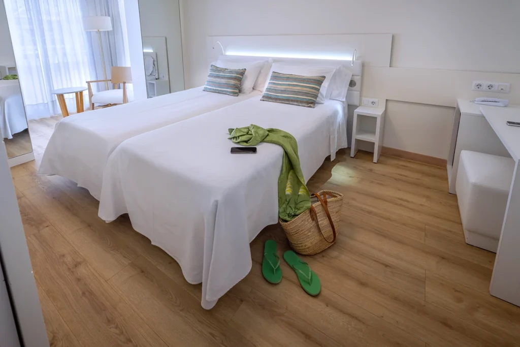 Habitaci&oacute;n con camas individuales, cojines azules decorativos y tonos suaves.