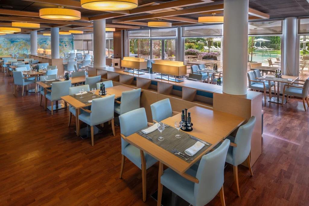 Restaurante moderno con sillas azules y mesas de madera junto a ventanas grandes.