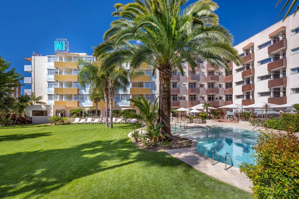 Edificio moderno con jard&iacute;n, palmeras y piscina.