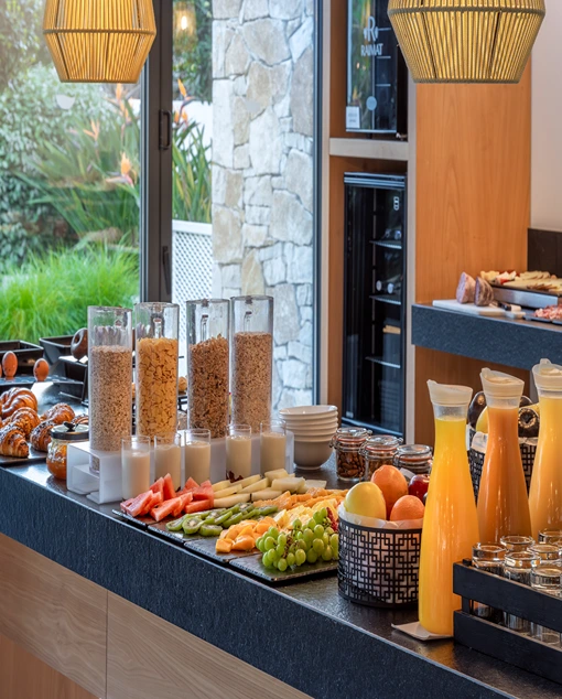 Mesa con desayuno variado de fruta, zumos y boller&iacute;a y vistas al jard&iacute;n.