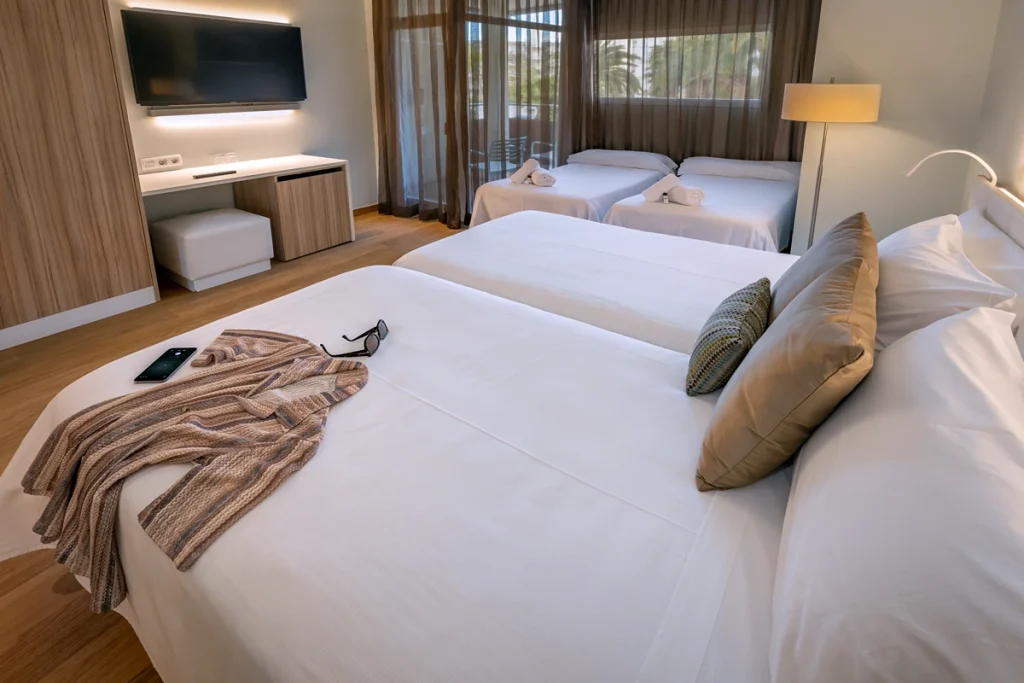 Habitaci&oacute;n con cuatro camas individuales, tonalidades suaves y vistas al jard&iacute;n.