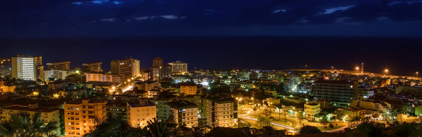 Vista nocturna de una ciudad con edificios iluminados y cielo oscuro nublado.
