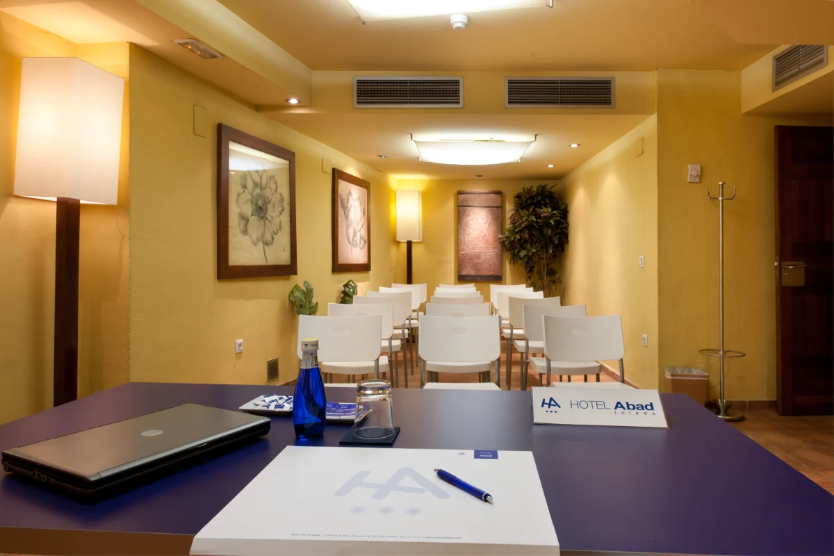 Sala de conferencias vacía con mesa, sillas blancas y decoración en pared.
