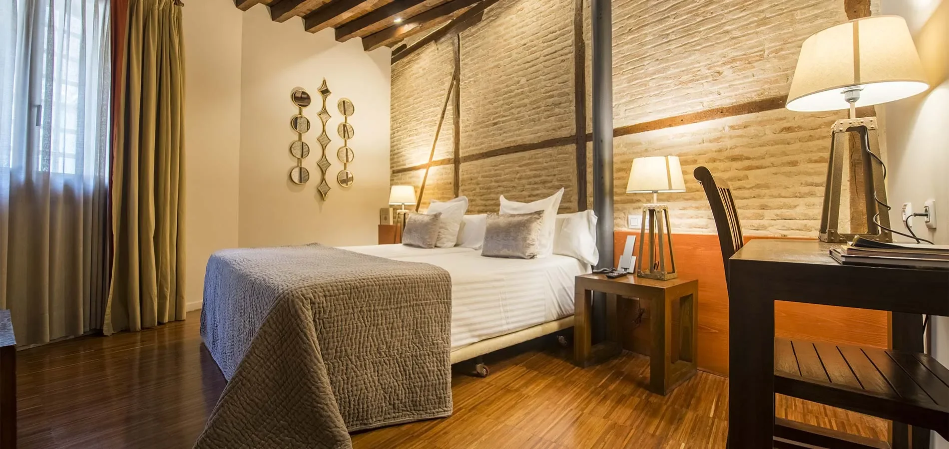 Habitaci&oacute;n r&uacute;stica con cama doble, l&aacute;mparas y detalles decorativos en la pared.