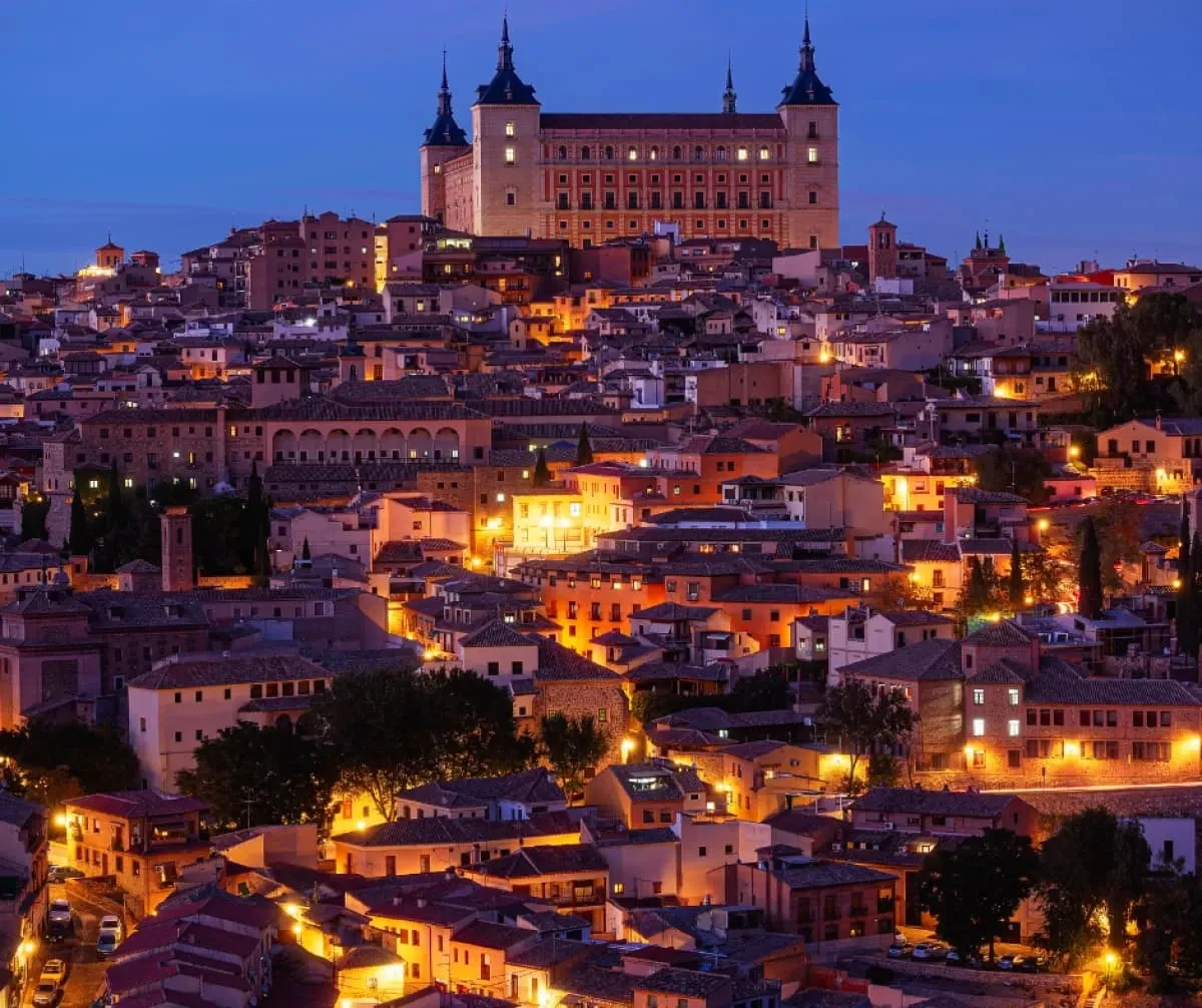 Vista nocturna de una ciudad iluminada con un gran edificio en el fondo.