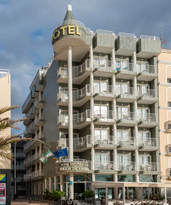 Hotel &ldquo;HO&rdquo; en edificio moderno junto a un paseo con palmeras y cielo azul