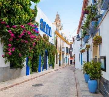 Calle estrecha andaluza con flores y casas blancas frente a la iglesia