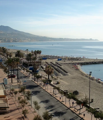 Playa con palmeras, paseo y vista del mar y la costa monta&ntilde;osa.