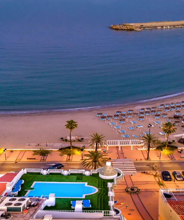Playa tropical con sombrillas y piscina junto al mar, vista a&eacute;rea al atardecer.