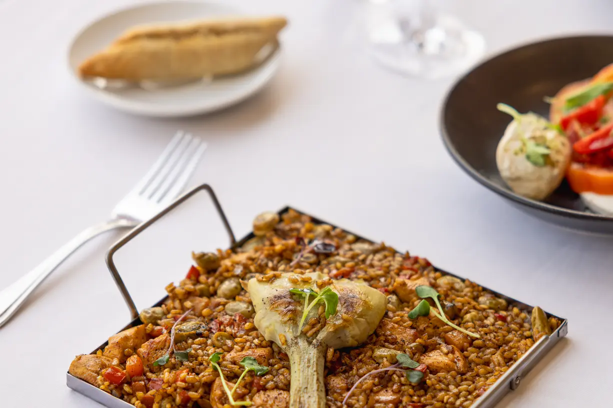 A delicious gourmet paella served on a stylish plate with a piece of artichoke.