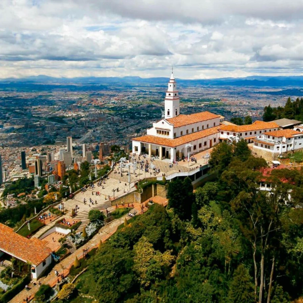 Iglesia blanca con campanario y tejado naranja sobre una ciudad vista panor&aacute;mica