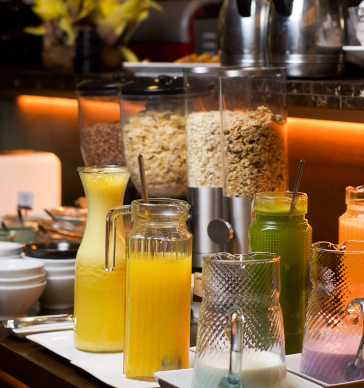 Mesa buffet con jugos y cereales en frascos de vidrio, en un caf&eacute;.