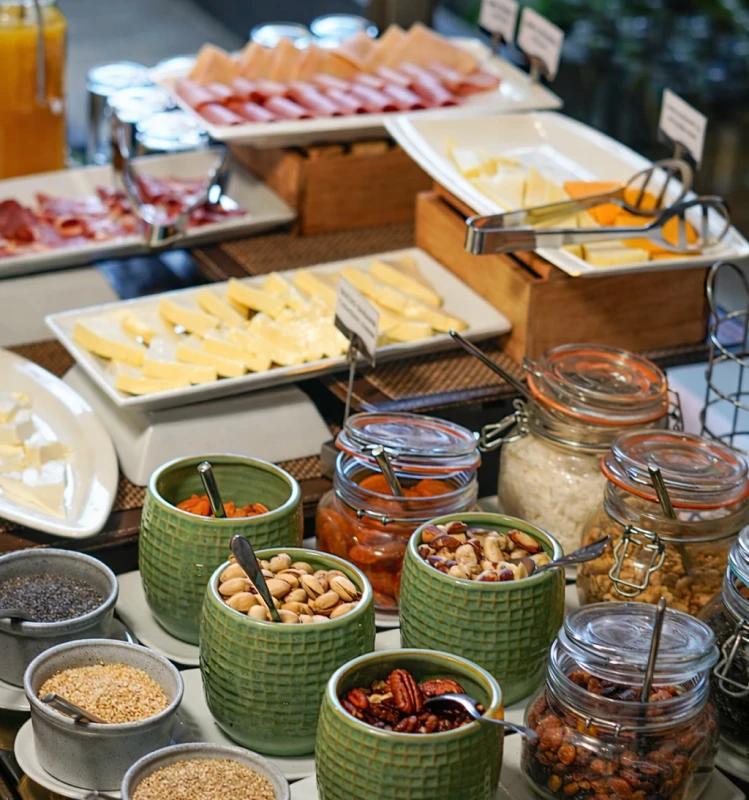 Mesa de buffet con quesos y fiambres, frascos de granos y frutos secos