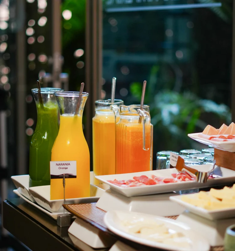 Bebidas en jarra y botellas con pajitas en buffet, fondo borroso.