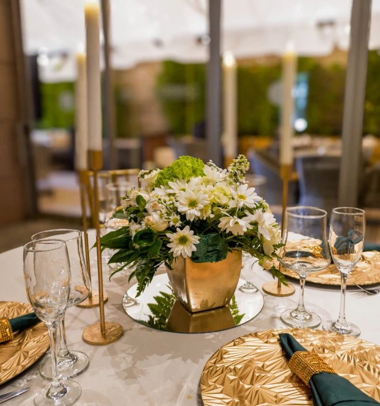 Centro de mesa con flores blancas y copas en mesa dorada para evento.
