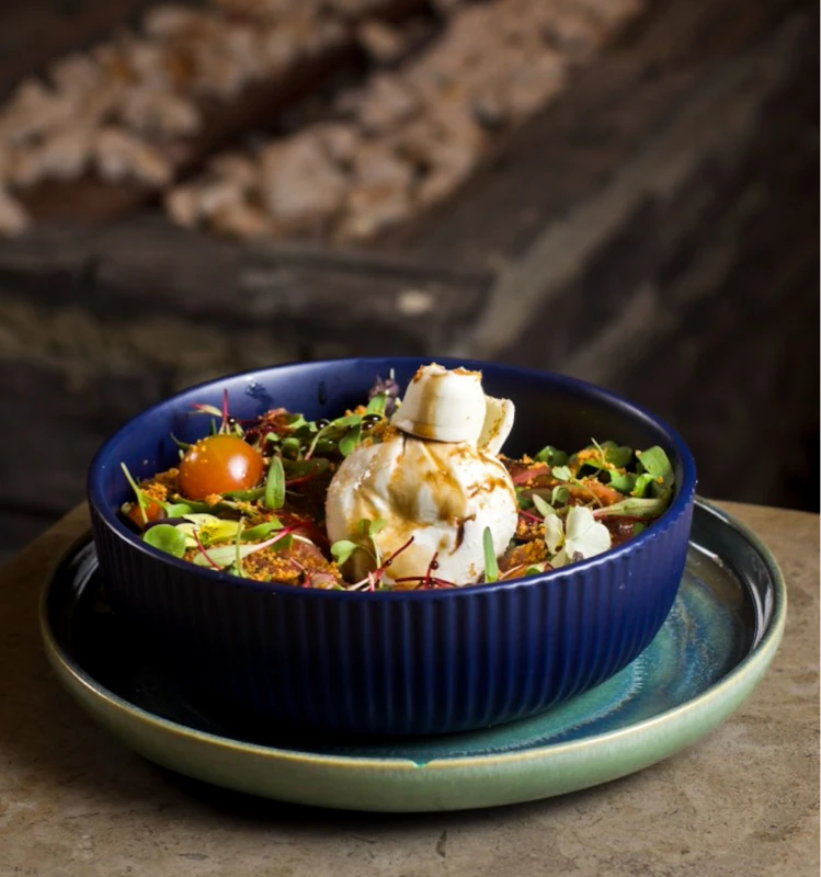 Ensalada servida en cuenco azul con queso y brotes sobre plato verde.