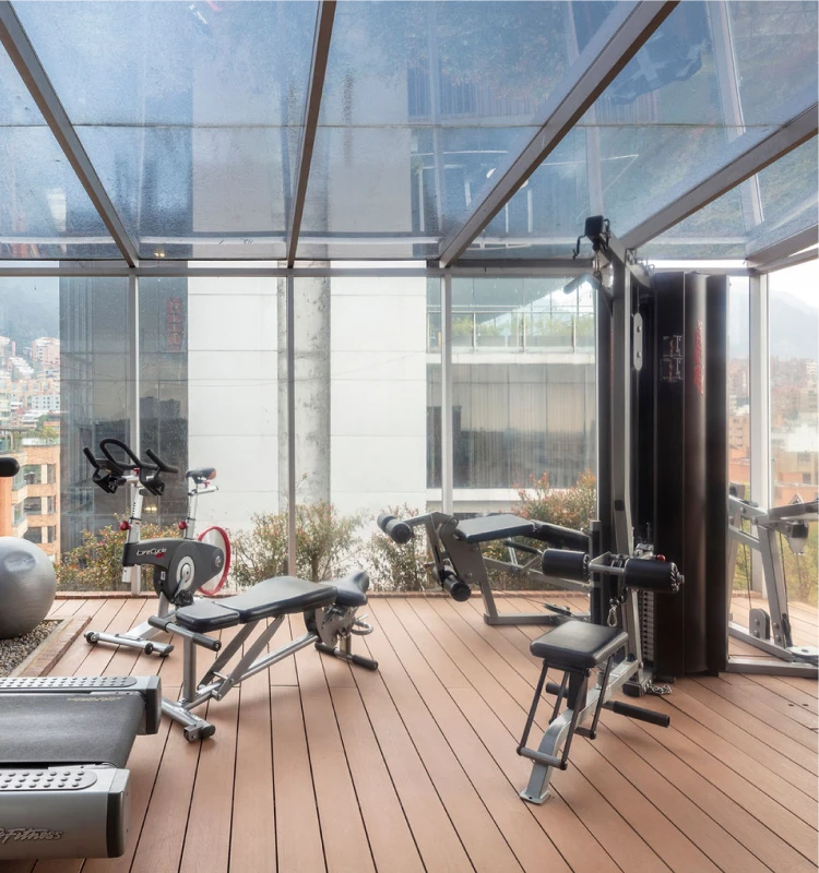 Gimnasio con m&aacute;quinas de ejercicio en terraza con vista urbana y ventanales
