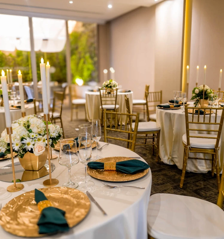 Mesa de banquete con velas, flores y vajilla en sala elegante.