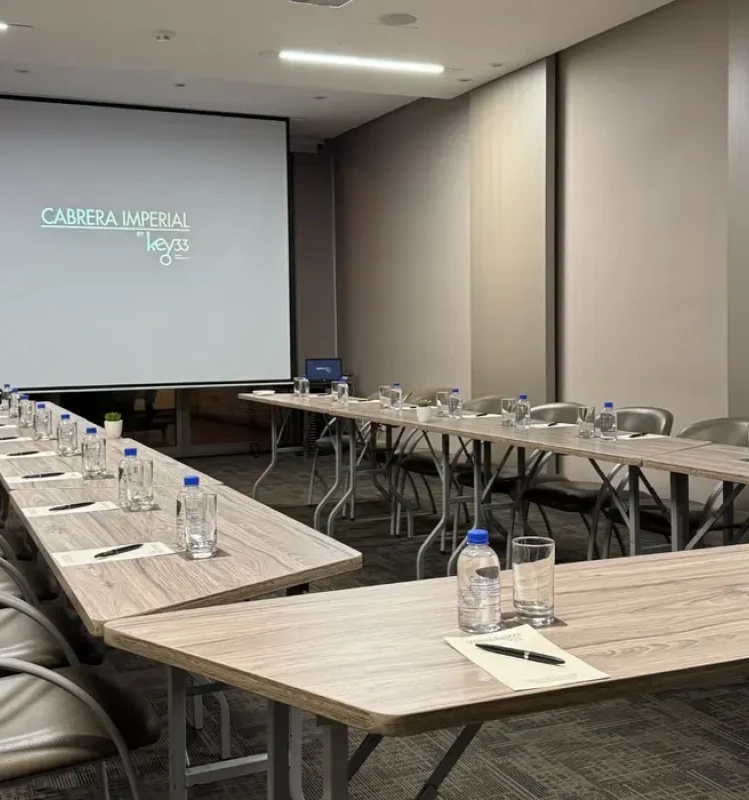 Sala de reuniones con mesas, sillas y proyector con logo &ldquo;Cabrera Imperial&rdquo;