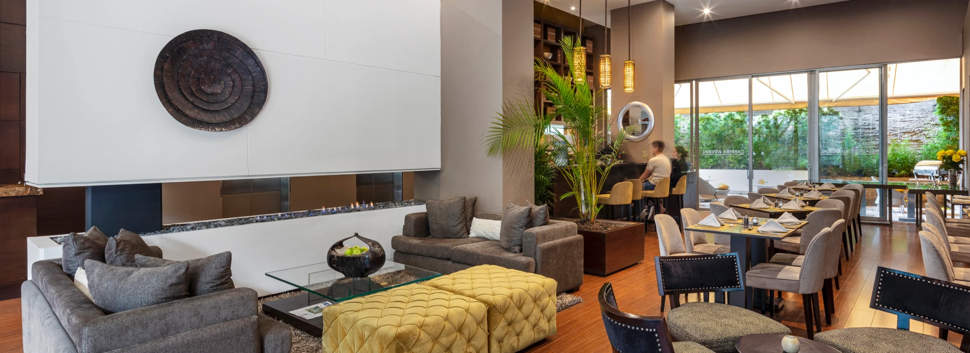 Sala de hotel moderna con chimenea, sof&aacute;s y mesa de comedor junto a ventanales