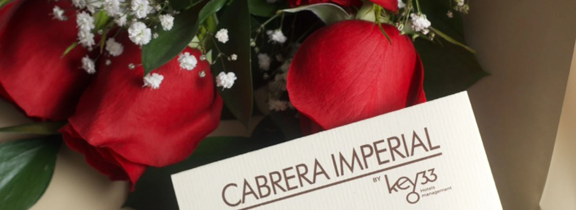Dos rosas rojas y tarjeta &ldquo;CABRERA IMPERIAL&rdquo; sobre hojas verdes