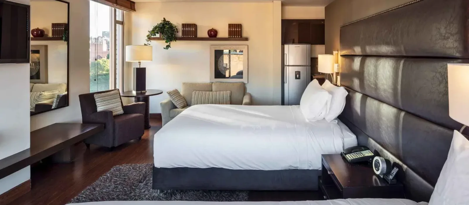 Habitaci&oacute;n de hotel moderna con cama doble, sala y estanter&iacute;as decorativas