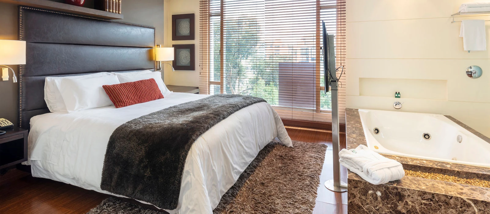 Dormitorio con cama doble, ventana con persianas y jacuzzi en suite hotelera
